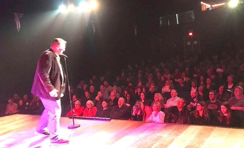 Eric Thompson commands the stage under dramatic purple lighting as he delivers his signature blend of comedy and magic to a packed theater audience, showcasing the engaging showmanship that has made him a favorite entertainer for decades.