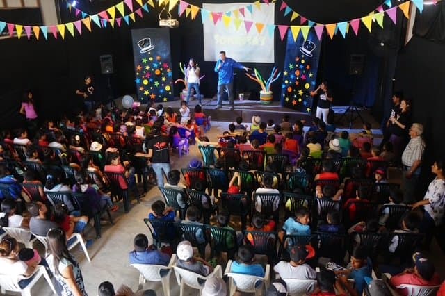 Eric Thompson captivates a packed audience of children and families in this vibrant venue decorated with colorful bunting and balloons. The master entertainer has the crowd's complete attention as he delivers what's surely another unforgettable performance filled with magic and comedy.