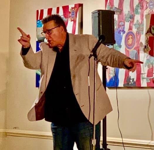 Eric Thompson commands the stage with animated gestures and infectious energy, working his magic on an appreciative audience at what appears to be a lively comedy performance.