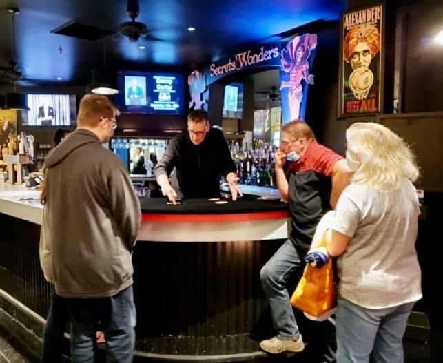 Eric Thompson captivates a small crowd at what appears to be a bar or restaurant venue, working his magic with an intimate audience gathered around him in the dimly lit space.