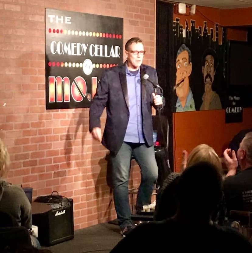Eric Thompson commands the stage at The Comedy Cellar, delivering his signature blend of humor to an intimate crowd of comedy fans in this classic brick-walled venue.