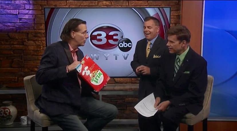 Eric Thompson brings his signature charm to a television interview, delighting the hosts with what appears to be a clever prop or magical surprise that has everyone grinning from ear to ear.