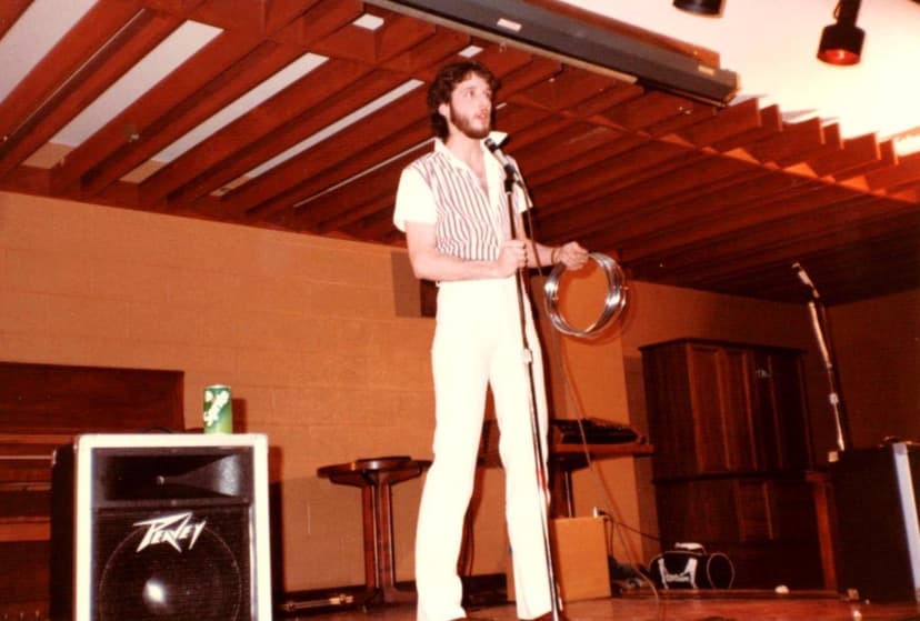 Eric Thompson takes the stage with his signature charm, working the microphone like a pro while his trusty drum awaits its moment in what looks like a cozy venue performance.