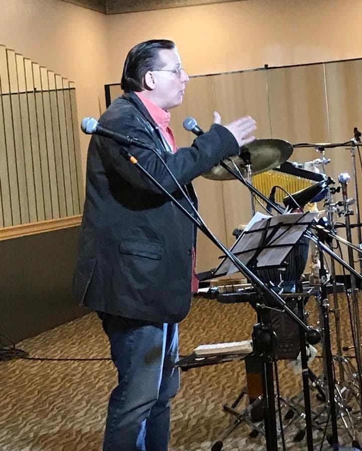 Eric Thompson commands the stage with animated gestures during what appears to be a lively performance, his enthusiasm clearly captivating the audience from behind his microphone setup.