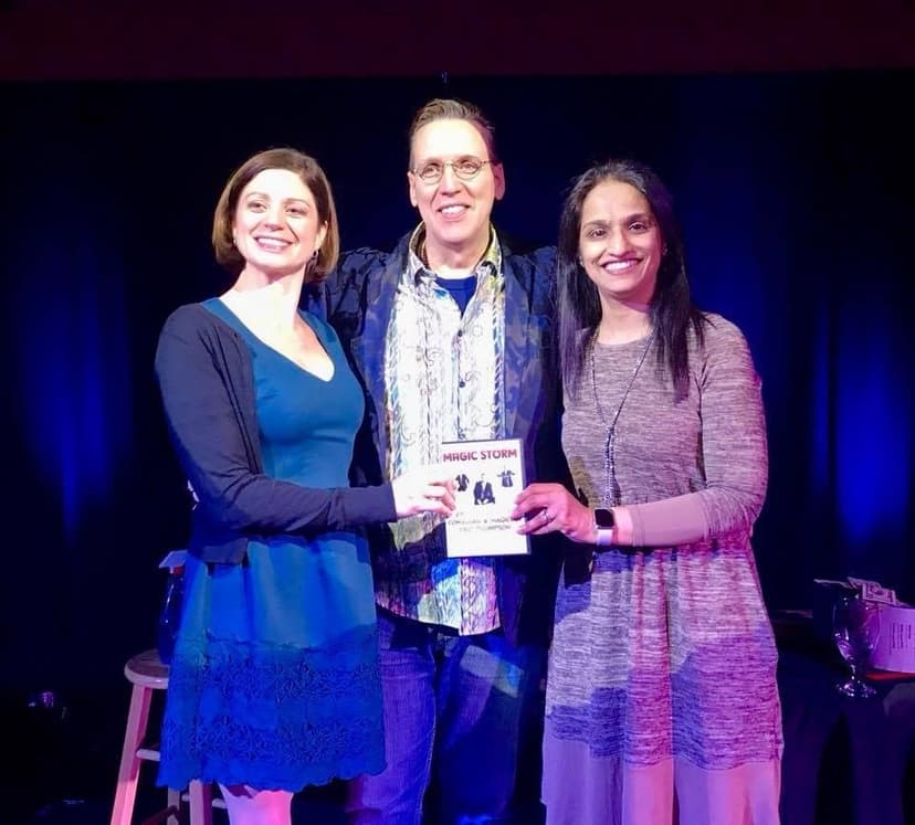 Eric Thompson celebrates with fans after what looks like a successful show, holding up what appears to be promotional material or a program while sharing smiles and laughs with audience members.