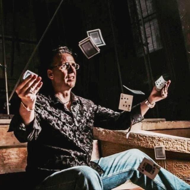 Eric Thompson showcases his magical prowess with a dramatic card manipulation, sending playing cards floating through the air in what appears to be a classic sleight-of-hand performance. The seasoned entertainer demonstrates the kind of theatrical flair that has made him a favorite at venues across the country for decades.