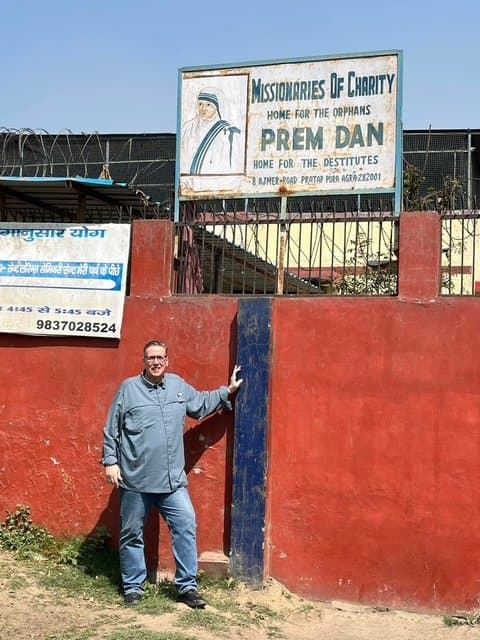 Eric Thompson takes a moment to pose during what appears to be a visit to the Missionaries of Charity's Prem Dan home for destitutes in India, showing his commitment to bringing joy and entertainment to communities around the world.