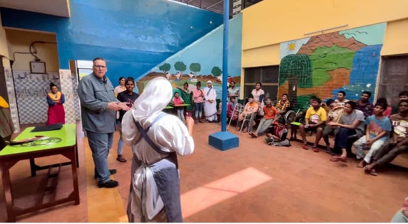 Eric Thompson captivates a diverse audience in what appears to be a community center or school, with colorful murals creating the perfect backdrop for his engaging performance.