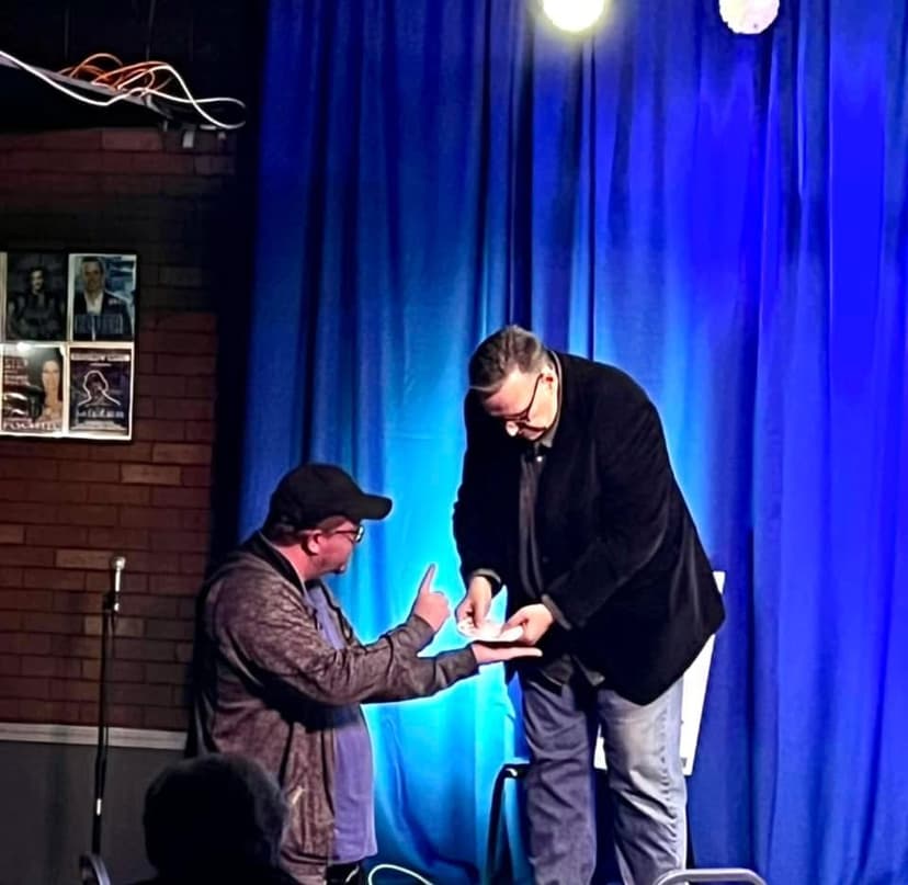 Eric Thompson takes a moment to sign an autograph for a fan, bringing his trademark warmth and personal touch to what appears to be a post-show meet and greet at an intimate comedy venue.
