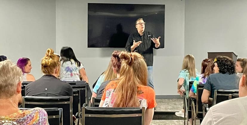 Eric Thompson captivates a classroom full of students during what appears to be an educational presentation, gesturing animatedly as his audience listens intently from their seats.
