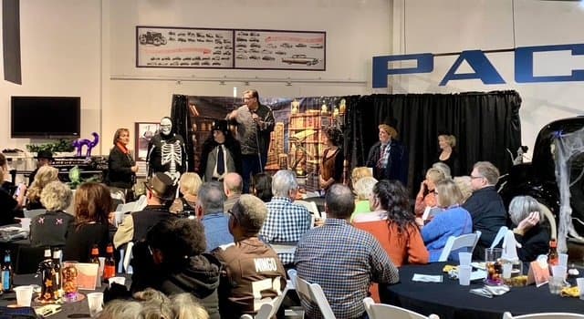 Eric Thompson captivates a seated audience during what appears to be a corporate or community event, working his magic from a small stage setup complete with props and backdrop.