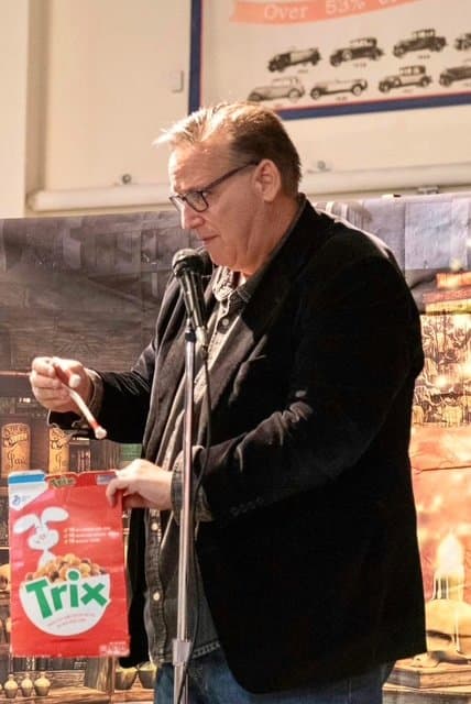 Eric Thompson brings his signature blend of comedy and magic to what appears to be a corporate event or fundraiser, complete with a colorful Trix cereal box as part of his engaging routine.