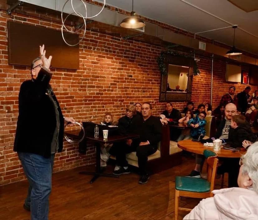 Eric Thompson captivates a packed coffee shop audience with his signature juggling routine, effortlessly keeping multiple rings aloft while delivering his comedic patter to the delighted crowd.