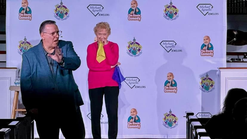 Eric Thompson brings audience members on stage for what looks like a hilarious interactive moment, with one participant covering their face in laughter or embarrassment while Eric works his comedic magic.