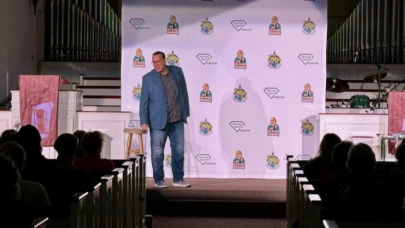 Eric Thompson takes the stage at what appears to be a church venue, working his comedic magic in front of an appreciative audience seated in traditional wooden pews.