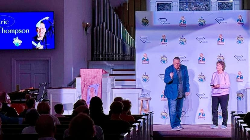 Eric Thompson takes the stage at what appears to be a church venue, with his image displayed prominently on the big screen as he prepares to entertain the packed audience with his signature blend of comedy and magic.