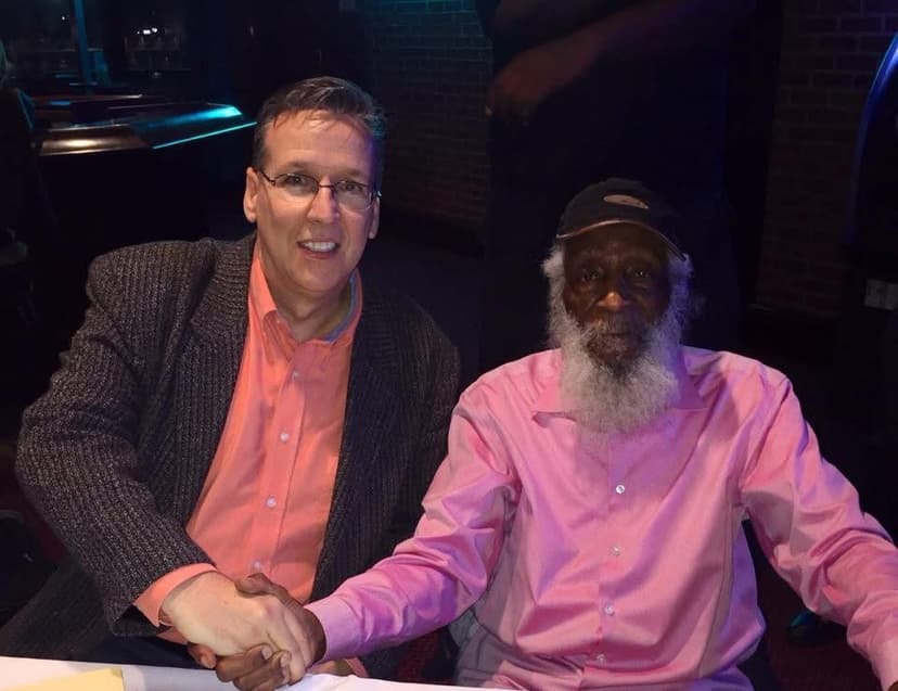 Eric Thompson shares a warm moment with a fellow performer, their genuine smiles and firm handshake capturing the camaraderie that makes live entertainment so special.