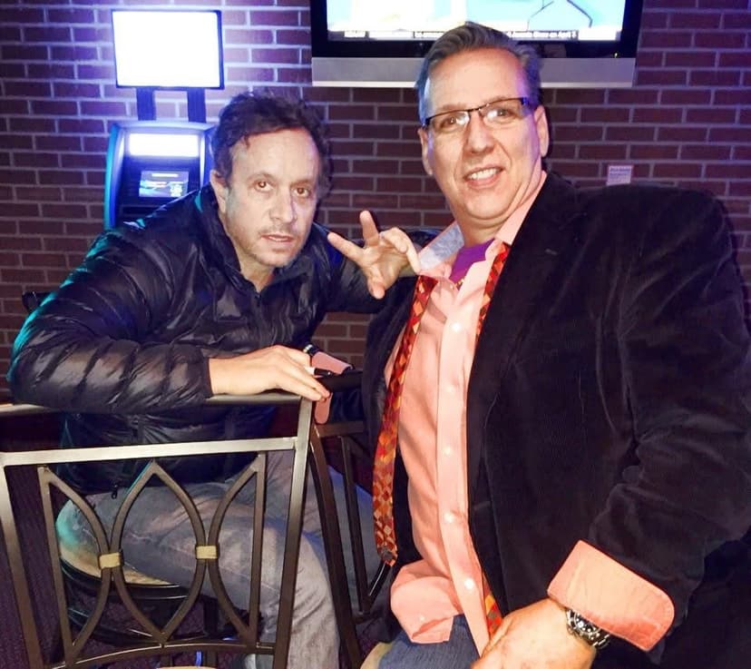 Eric Thompson shares a friendly moment with a fellow entertainer at what appears to be a comedy club or entertainment venue, both clearly enjoying the backstage camaraderie that comes with the business.
