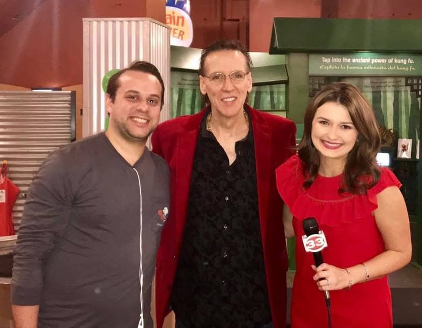 Eric Thompson strikes a pose with fellow entertainers during what appears to be a media interview or backstage meet-and-greet, showing off his signature showman style in that eye-catching red jacket.