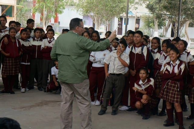 Eric Thompson captivates a crowd of uniformed school children during what appears to be an entertaining educational performance, with the kids clearly engaged and excited by his showmanship.