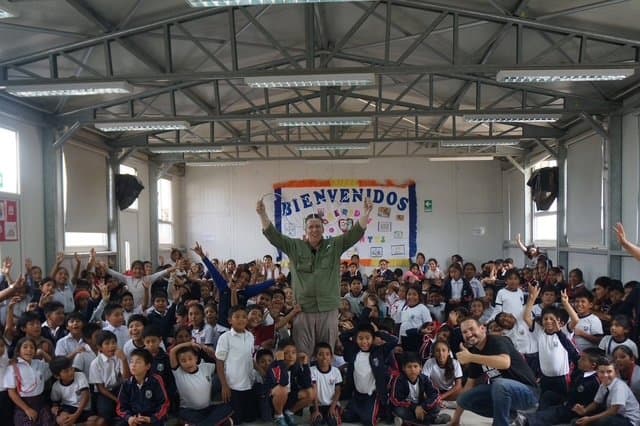 Eric Thompson energizes a packed auditorium of enthusiastic students, his arms raised triumphantly as the young crowd waves and cheers during what appears to be an unforgettable school assembly performance.