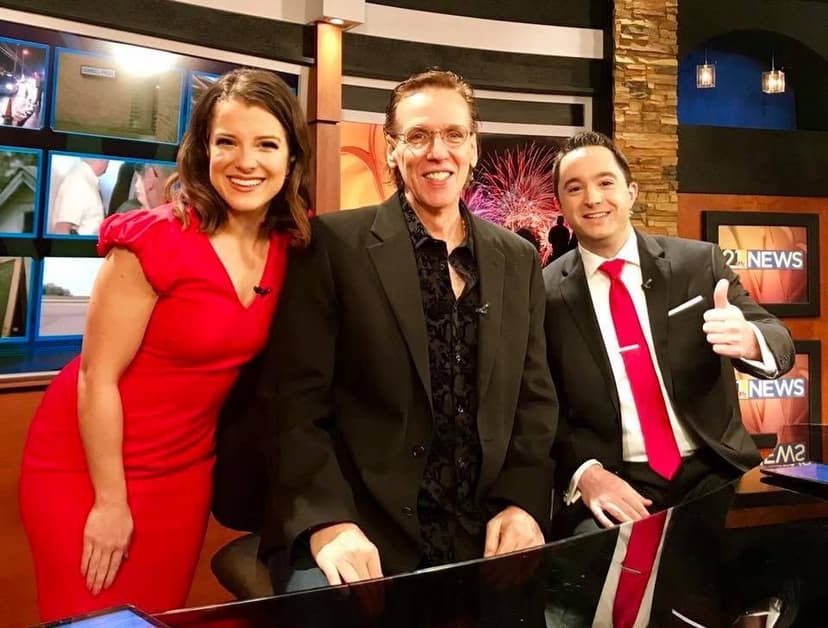 Eric Thompson strikes a pose with the news team during what appears to be a fun television appearance, bringing his signature warmth and showmanship to the studio set.