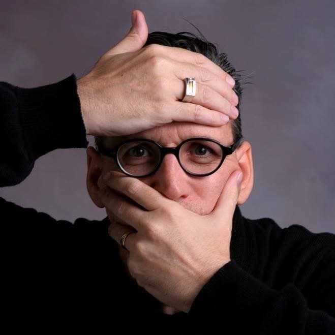 Eric Thompson strikes a playful pose with his hands framing his face, showing off his signature humor and expressive personality that has delighted audiences for decades.