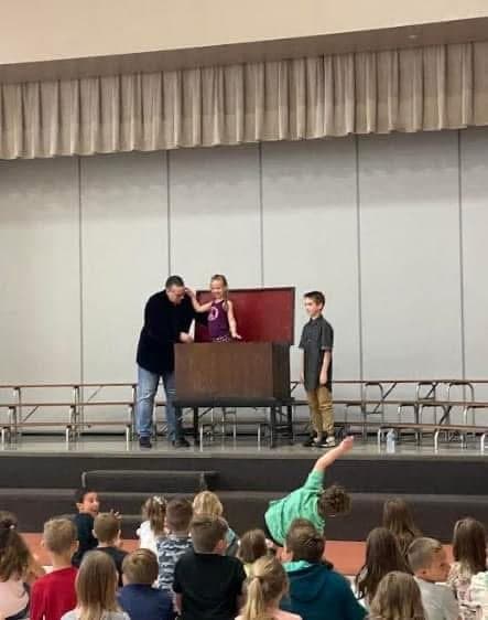 Eric Thompson captivates a young audience from the stage, working his magic with what appears to be a classic comedy routine involving audience volunteers.