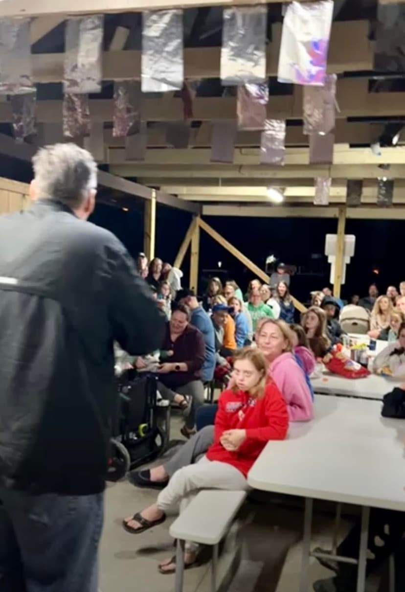 Eric Thompson captivates a packed audience from the stage, working his magic on an engaged crowd seated at tables in what appears to be a lively venue performance.