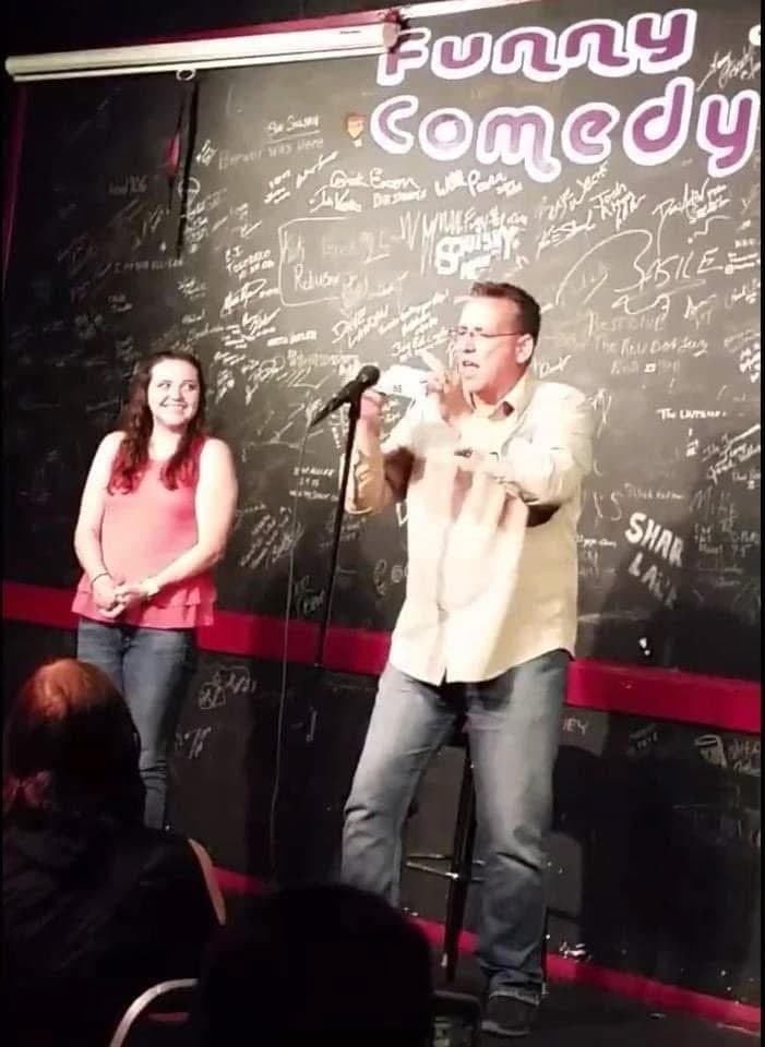 Eric Thompson brings an audience member on stage during his comedy show, sharing a laugh as he works his signature blend of humor and audience interaction at what appears to be a packed comedy club.