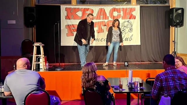 Eric Thompson takes the stage at what appears to be a comedy club, sharing the spotlight with a fellow performer as they work the intimate crowd with his signature warm, engaging style.