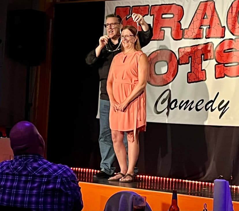 Eric Thompson brings an audience member on stage for what's sure to be a hilarious bit at this intimate comedy club, with both performer and volunteer sharing genuine laughs under the bright stage lights.