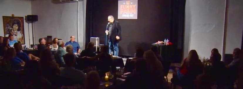 Eric Thompson commands the stage at an intimate comedy club, delivering his signature blend of humor and charm to a captivated audience seated at cozy tables.