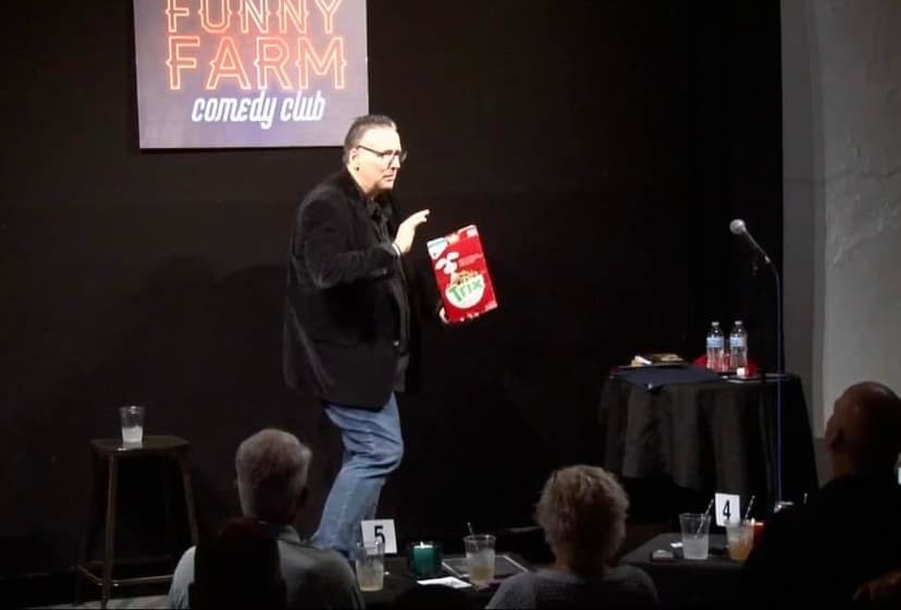 Eric Thompson delights the intimate crowd at the Funny Farm comedy club, holding up a festive prop that's sure to get some laughs during his engaging performance.