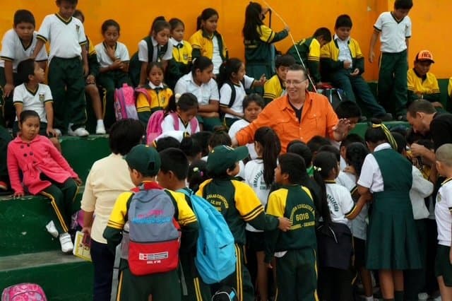 Eric Thompson captivates a group of enthusiastic school children during what appears to be an educational assembly, with the kids gathered around him in rapt attention as he works his magic.