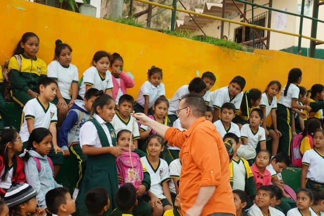 Eric Thompson captivates a young audience during what appears to be a school performance, engaging directly with enthusiastic students seated on colorful bleachers. The kids are clearly enthralled as Eric works his magic and comedy skills in this intimate educational setting.