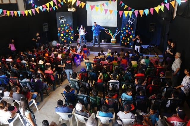 Eric Thompson captivates a packed audience of children and families at what appears to be a festive community event, with colorful bunting and decorations creating the perfect backdrop for his entertaining performance.