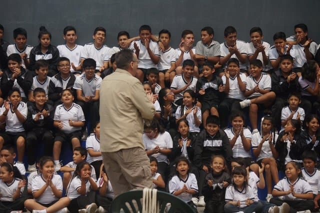 Eric Thompson captivates a sea of uniformed students during what appears to be a school assembly, working his comedic magic as the young audience hangs on his every word and gesture.