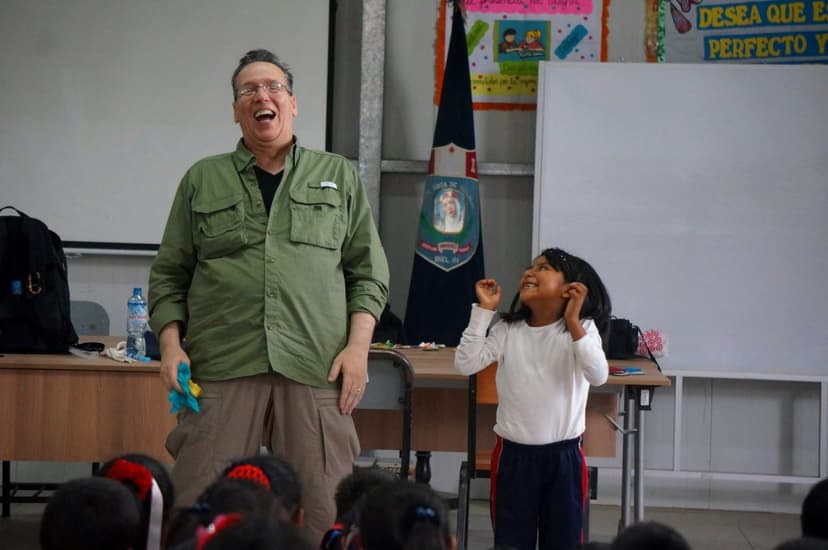 Eric Thompson brings his signature warmth and humor to a classroom full of delighted students, sharing a genuine moment of laughter with a young participant who's clearly enjoying every second of the show.
