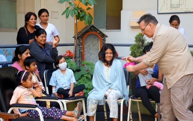 Eric Thompson brings his signature warmth to what appears to be a community gathering or fundraiser, delighting a seated audience that includes children and families in this intimate outdoor setting.