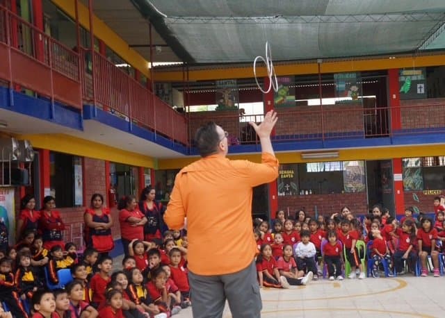 Eric Thompson captivates a packed audience of enthusiastic children at what appears to be a school assembly, juggling rings while the young crowd watches in delighted anticipation.