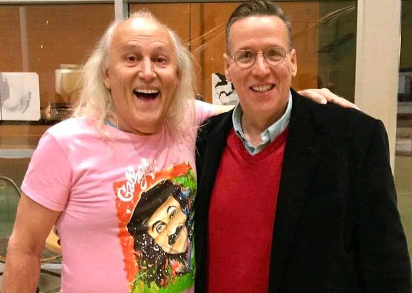 The ever-entertaining Eric Thompson shares a laugh and friendly moment with a fellow performer or fan, both grinning from ear to ear in what appears to be a casual backstage or venue meeting.
