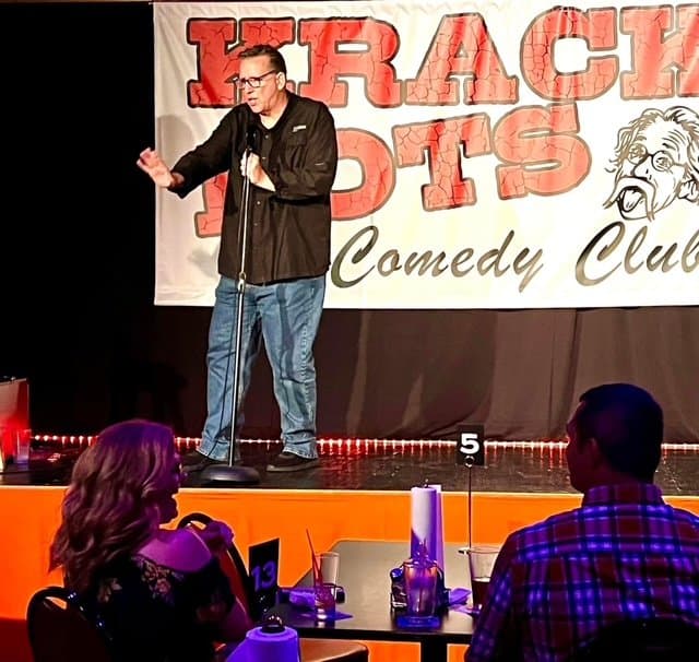 Eric Thompson commands the stage at a comedy club, delivering his signature blend of humor to an intimate audience gathered around candlelit tables.