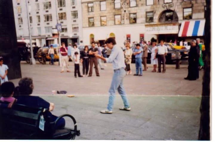 Eric Thompson commands attention in what appears to be a European town square, entertaining a gathering crowd with his signature blend of comedy and magic while onlookers pause to enjoy the impromptu street performance.