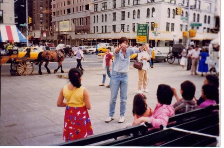 Eric Thompson captivates a street crowd with his magic and comedy, turning a busy city corner into an impromptu outdoor theater where horse-drawn carriages and curious onlookers create the perfect backdrop for his entertaining performance.