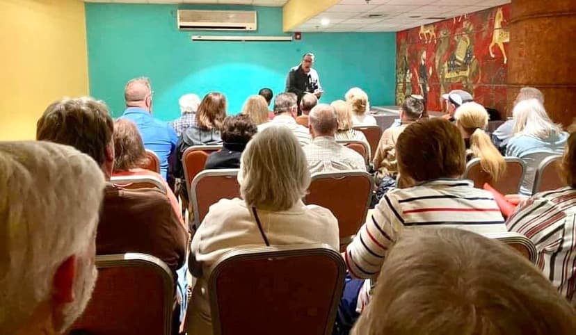 Eric Thompson captivates a packed audience during what appears to be a community center or church presentation, with attendees of all ages hanging on his every word as he delivers his signature blend of comedy and magic.