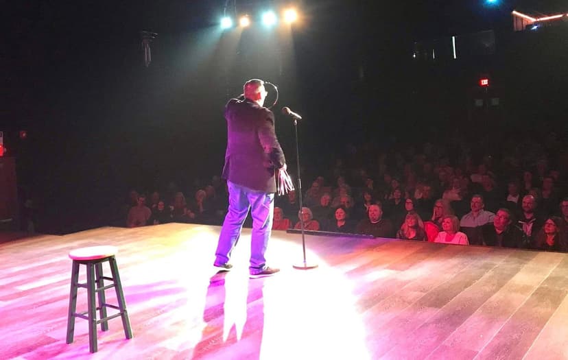 Eric Thompson commands the stage under dramatic purple lighting, delivering his signature blend of comedy and magic to a packed theater audience.