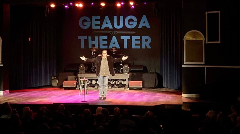 Eric Thompson commands the stage at the Geauga Theater, arms spread wide as he connects with his audience in this intimate venue setting.