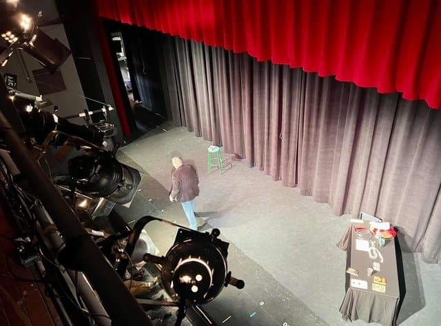 Eric Thompson commands the stage from above as he prepares for another crowd-pleasing performance, with professional lighting and camera equipment capturing every moment of his theatrical magic.