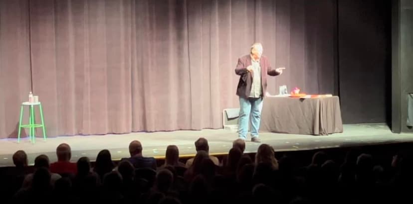 Eric Thompson commands the stage with his signature warmth and charisma, working his magic on an engaged theater audience from behind his performance table setup.